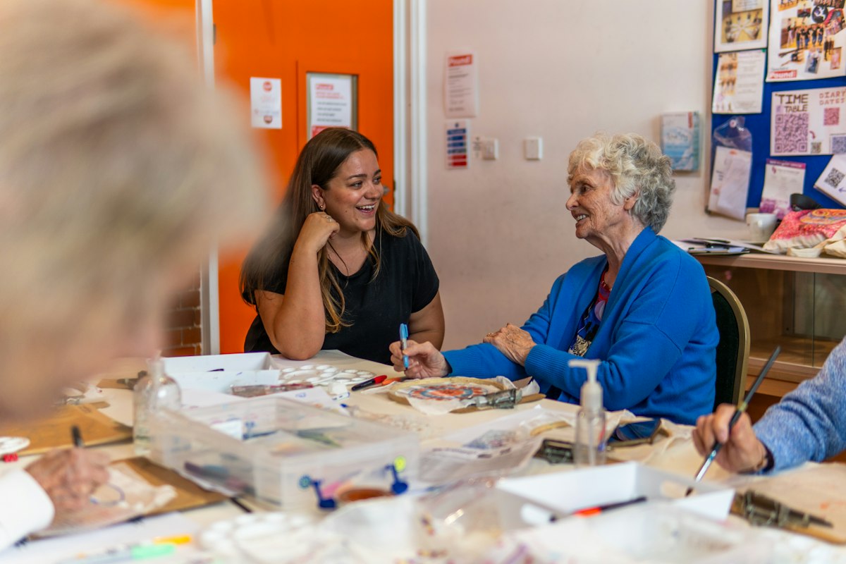 A young woman and an older woman chatting and laughing at a community art class