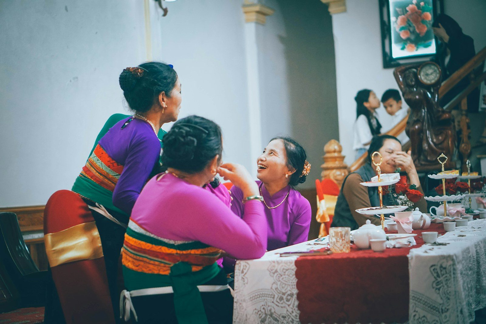 Women in colourful traditional dress talking and laughing around a table set for tea